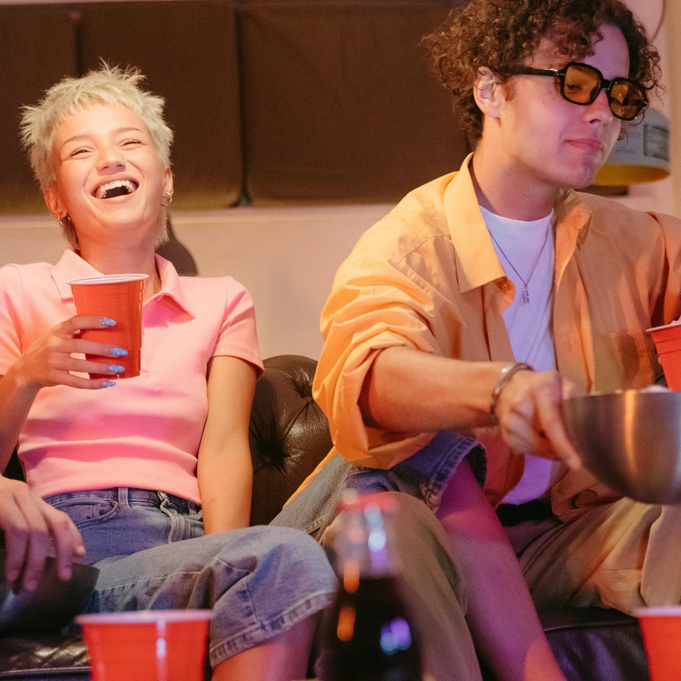 Young woman laughing on couch holding a cup and sitting with friends