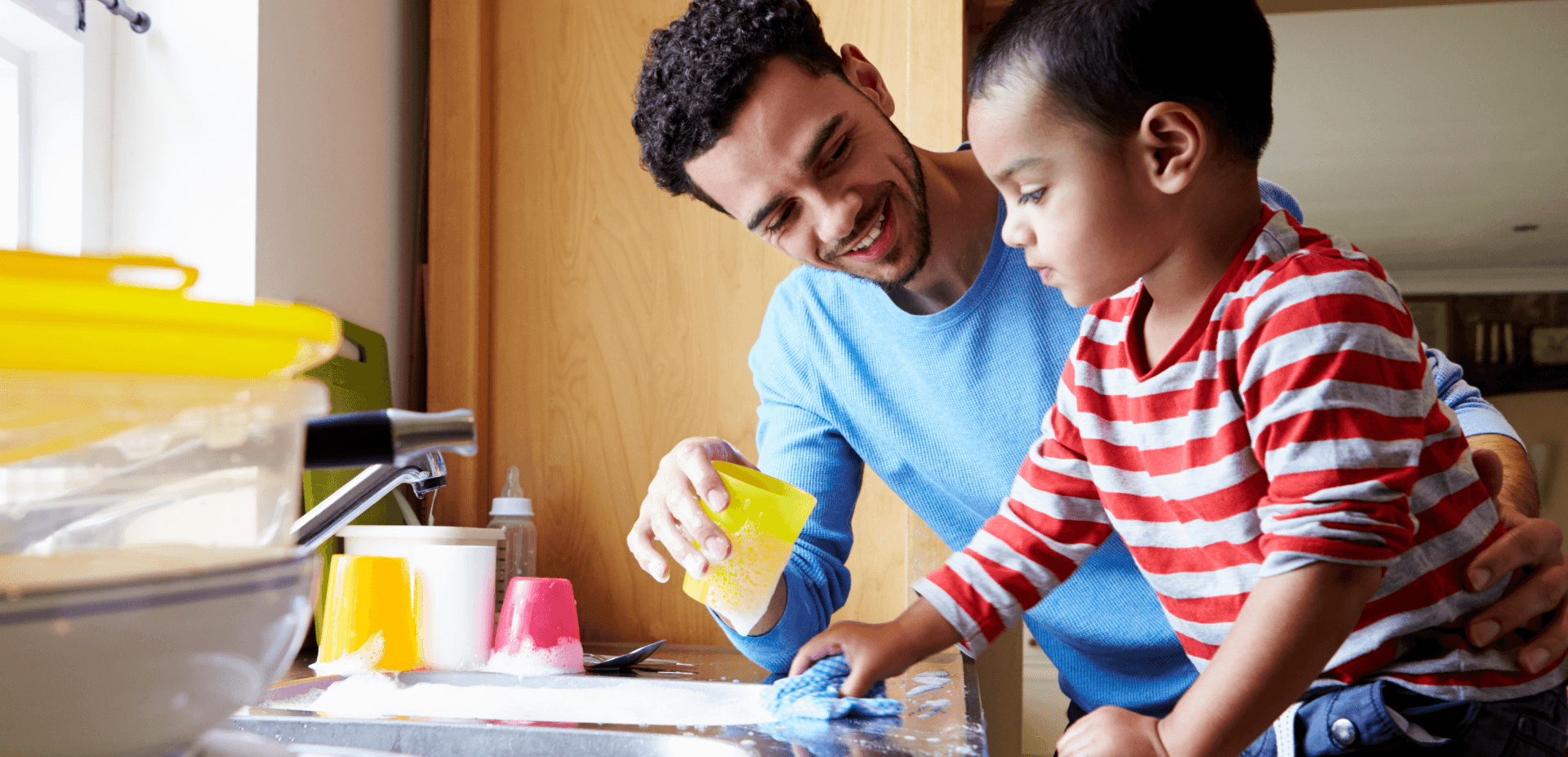 Dad and young boy at sink washing dishes