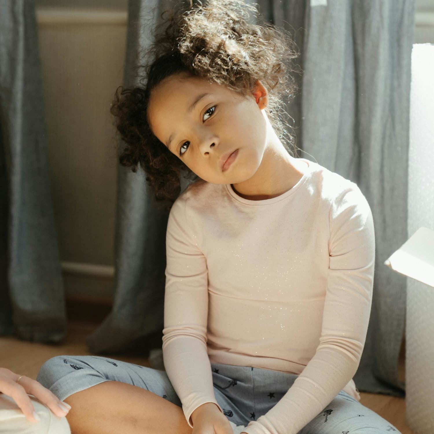 Young girl sitting on the floor, head tilted to the side, looking at the camera