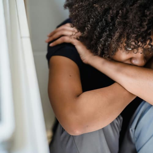 Young woman of color sitting with arms crossed looking off to side with her head down