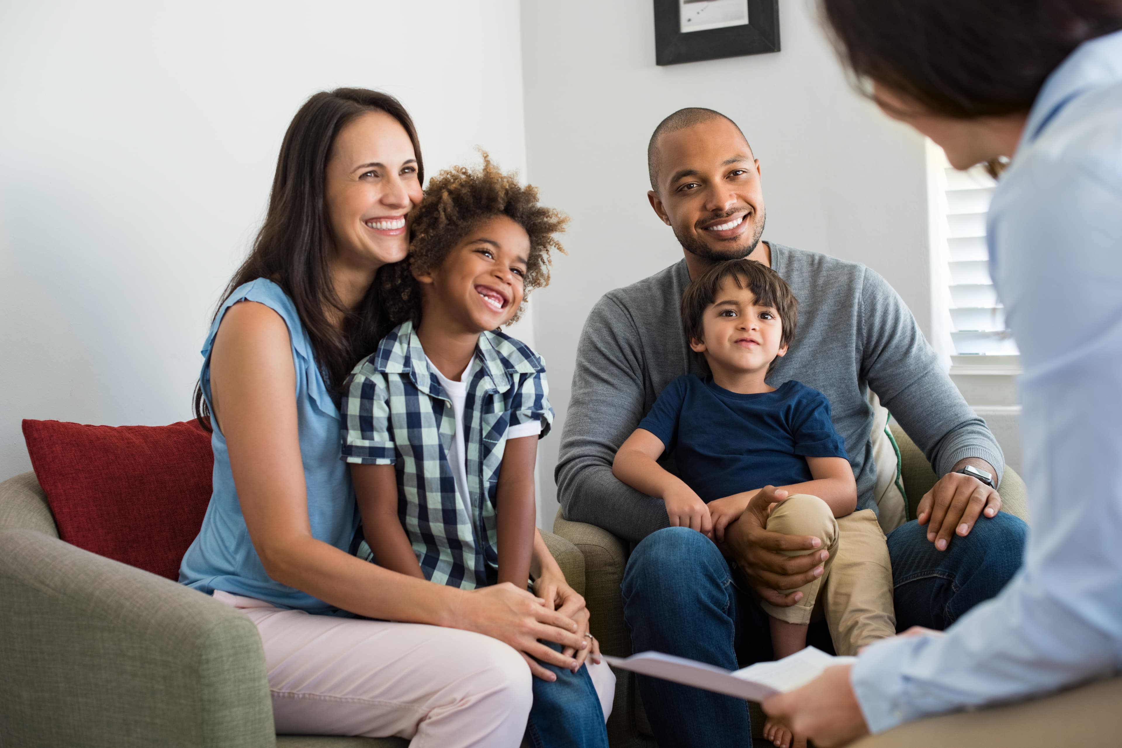 Two smiling parents sit on a couch with their two kids all looking at a therapist