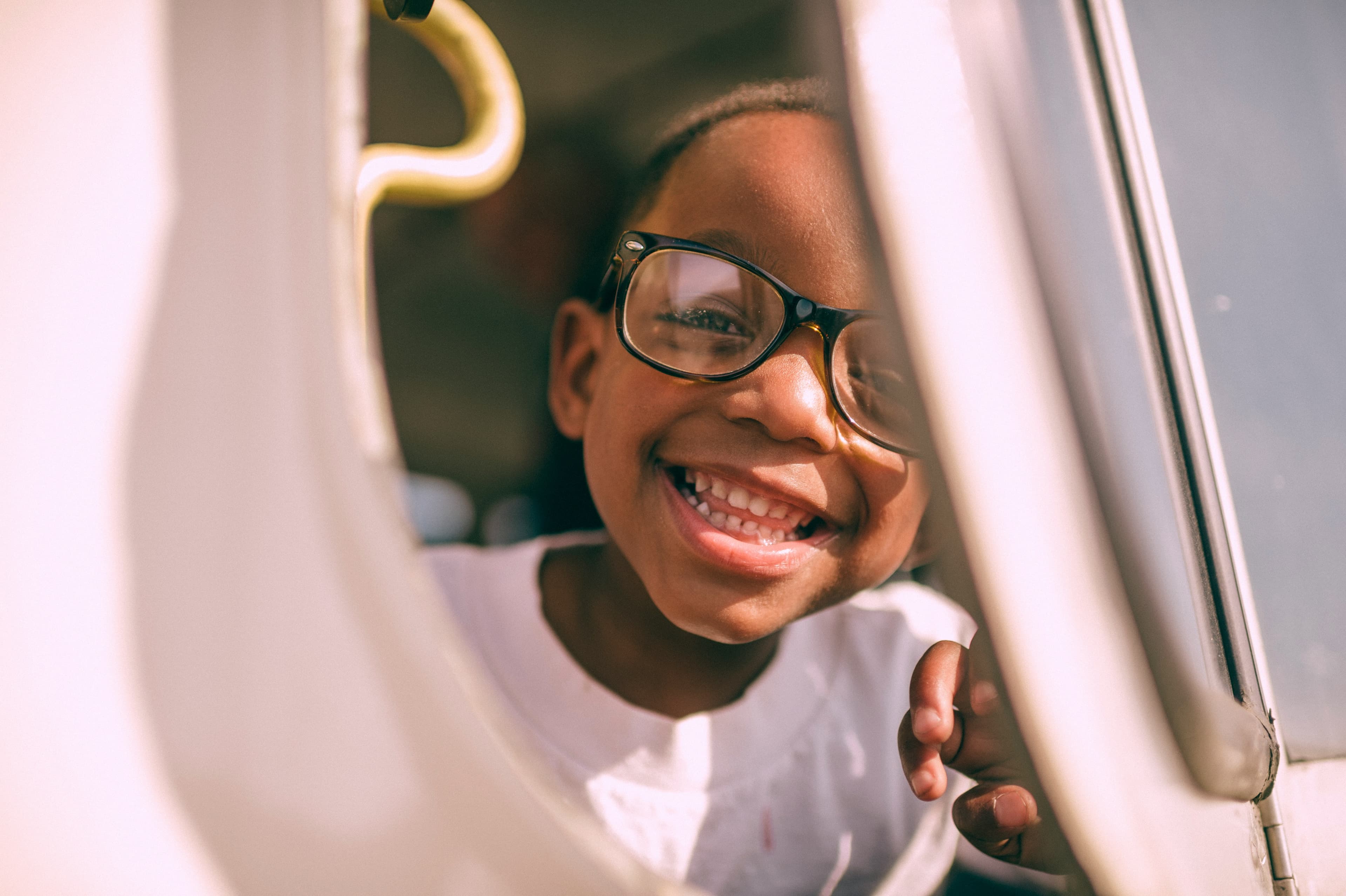 Smiling young boy with glasses on looking out of a window he's holding open