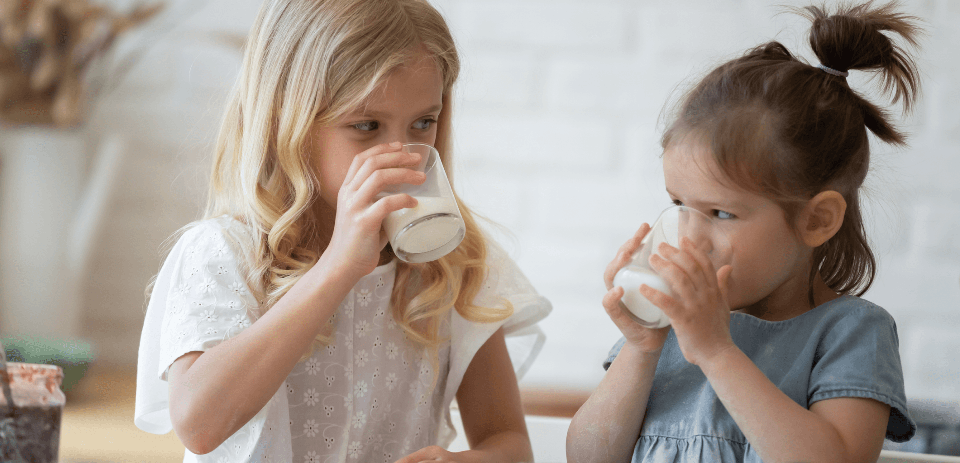 Two young girls each drinking a glass of milk and looking at each other
