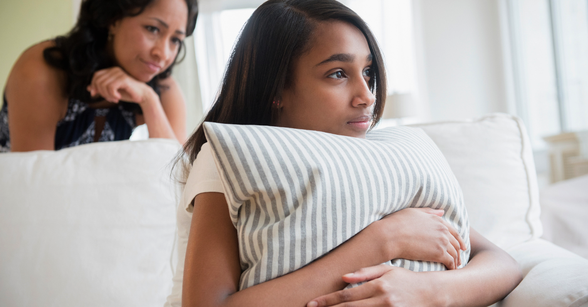 Concerned mother behind teen hugging pillow on couch
