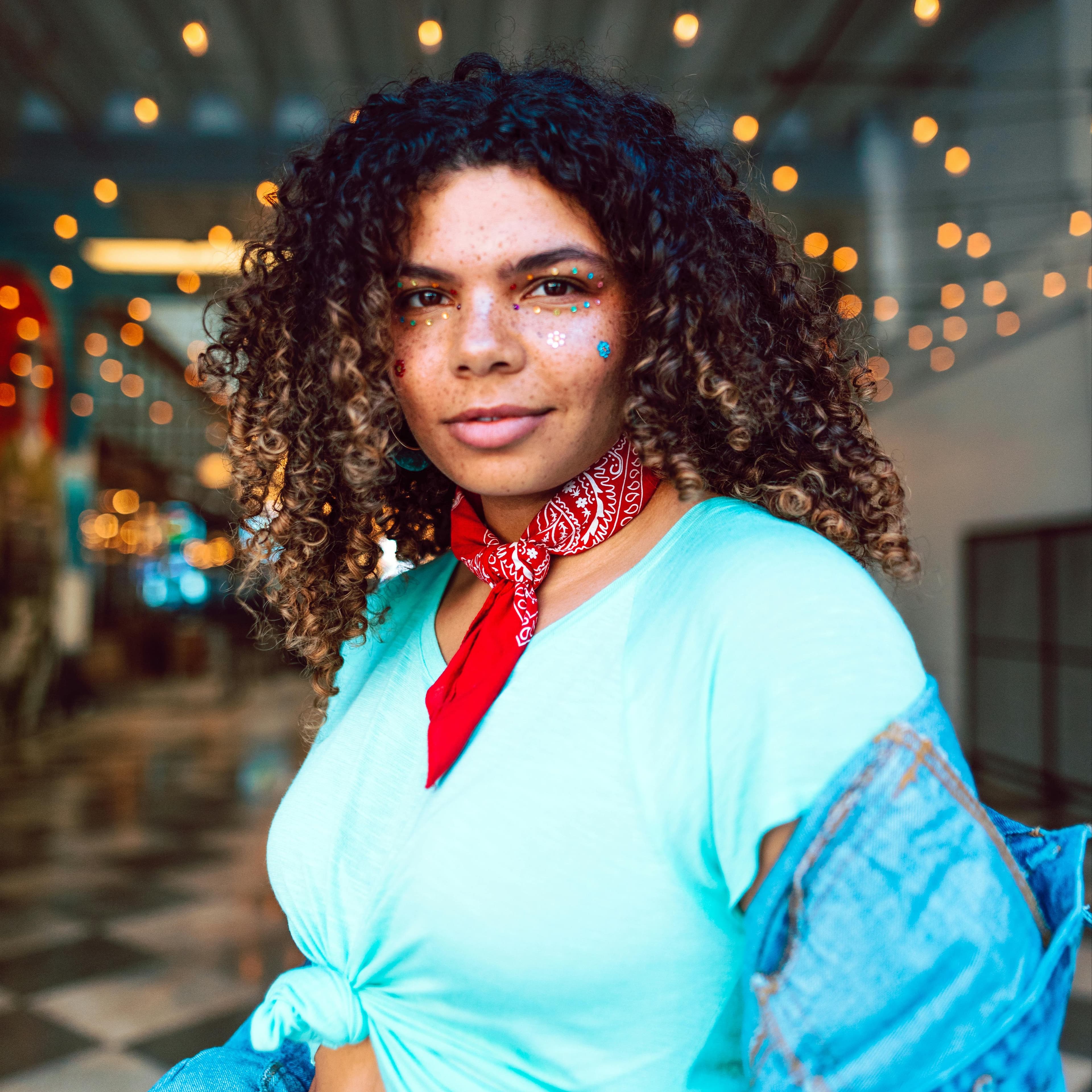 Young woman with sparkles on her face and a red bandana around her neck looks at the camera with a smile