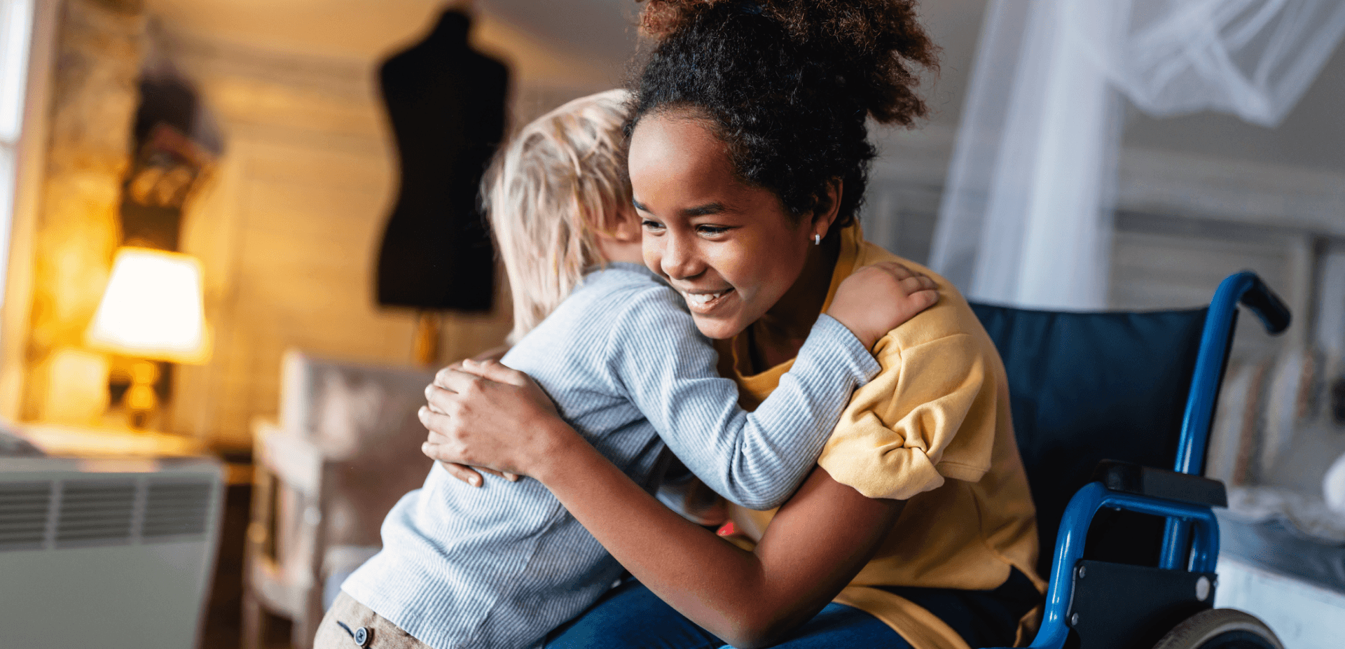 Young blonde child hugging a smiling Black child in a wheelchair